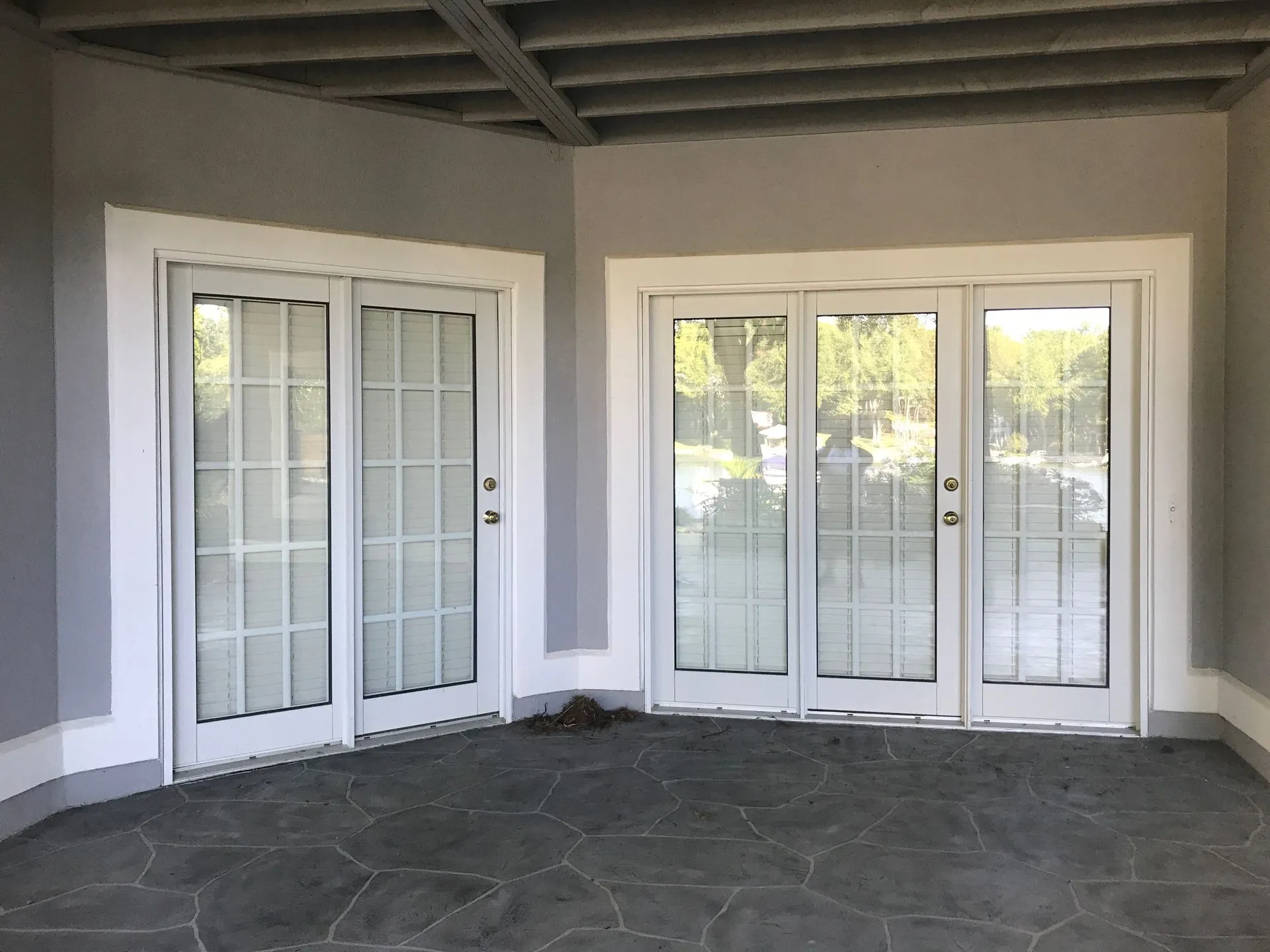 Two white french doors with white trim in a gray-walled corner on a gray stone patio.