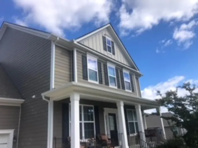 Two-story house with gray siding, white trim, porch, and blue sky with clouds.