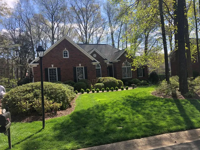 Brick house with a manicured lawn, shrubs, and trees under a sunny sky.