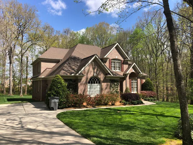 Brick house with brown roof and landscaping; driveway and trees.