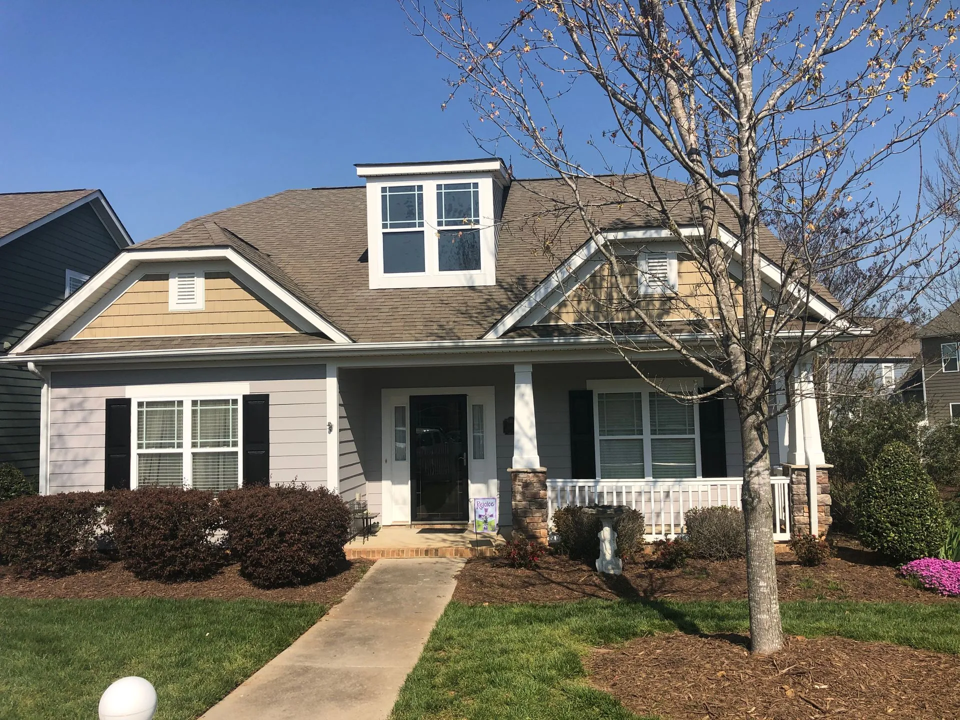 Tan and gray house with black shutters, a small porch, and a dormer window.