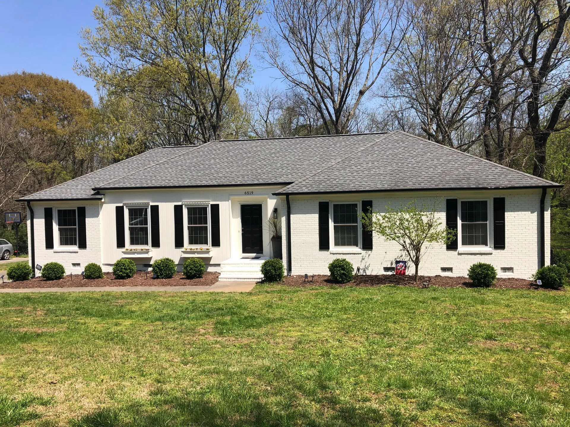 White brick ranch-style house with black shutters, gray roof, and green lawn.