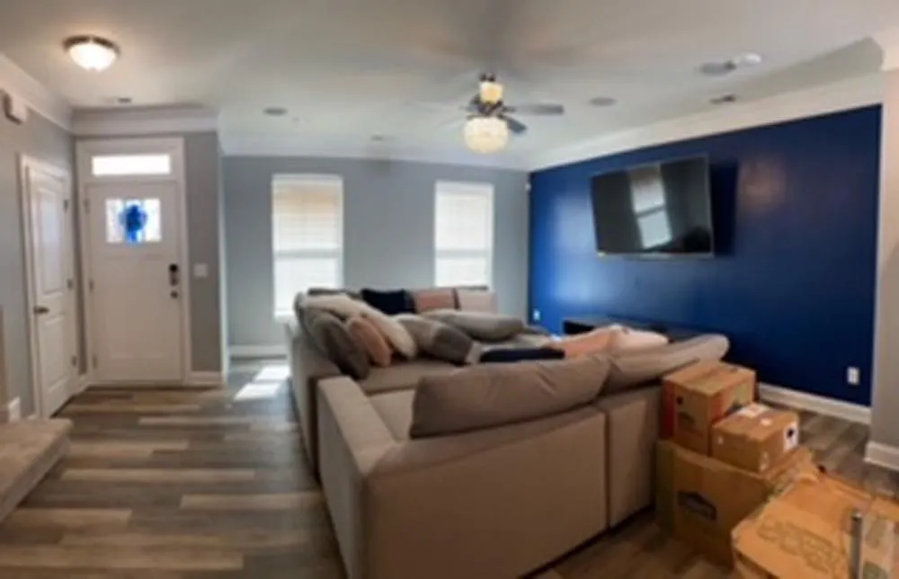 Living room with sectional sofa, TV, and blue accent wall. Boxes are stacked in the corner.