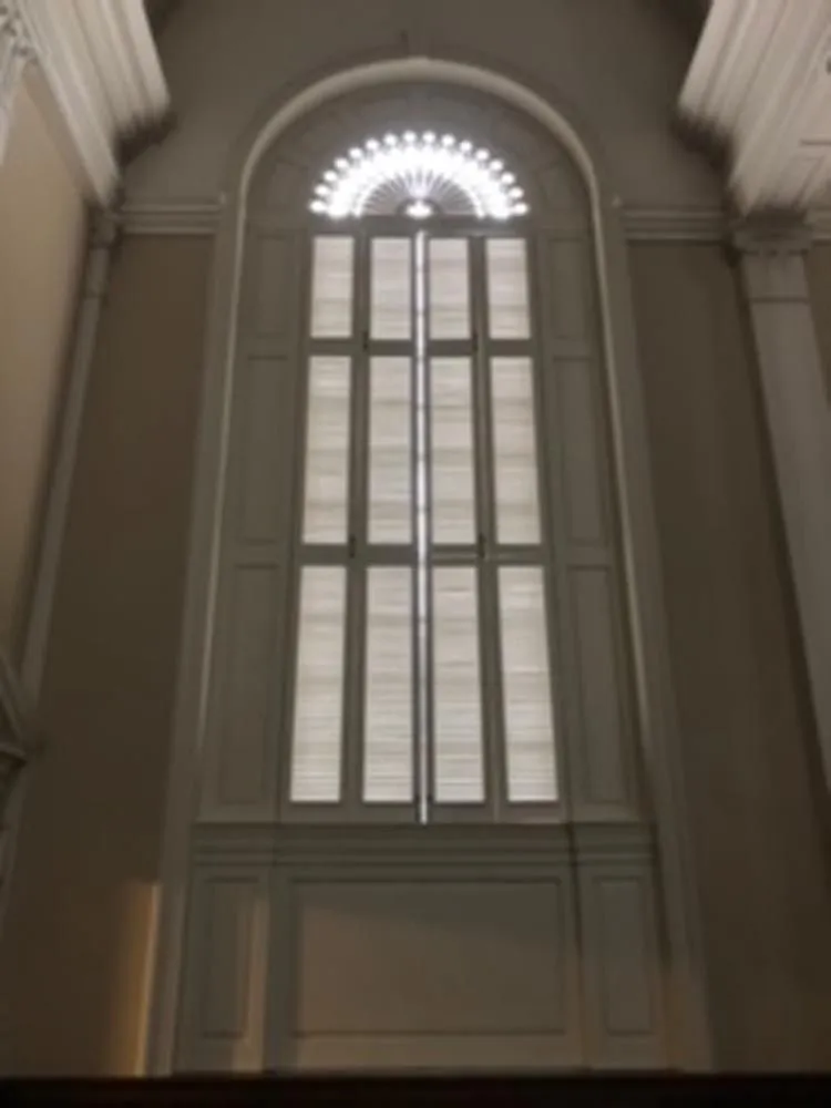 Tall arched window with white frame and blinds, in a cream-colored room.