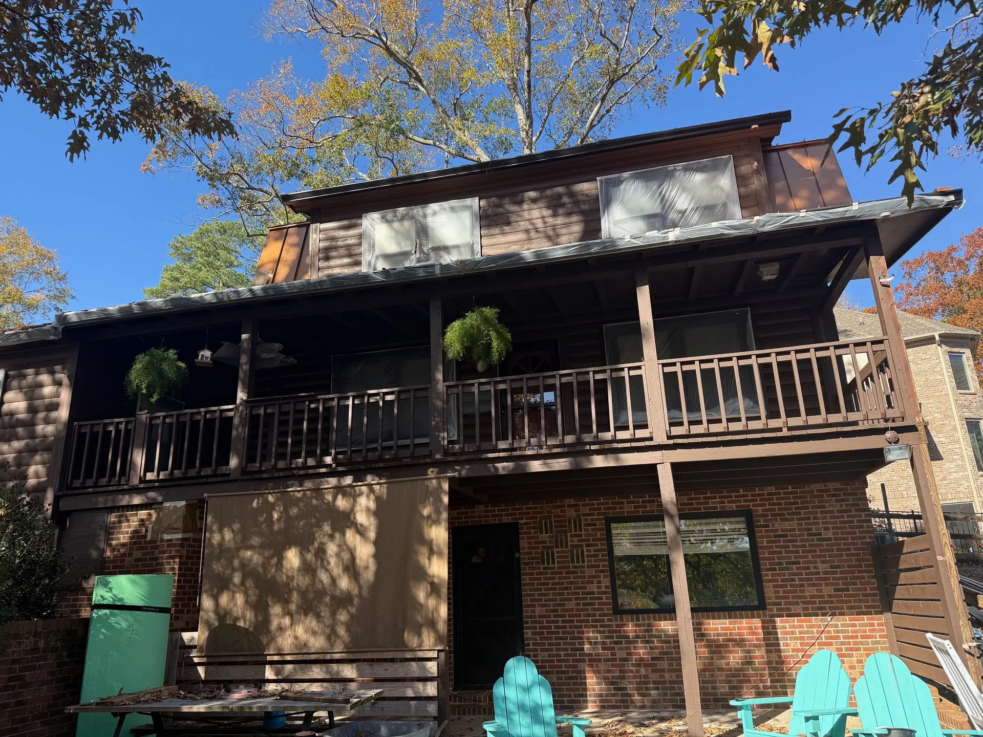 Two-story cabin with brown wood and brick exterior, balconies, and hanging plants.