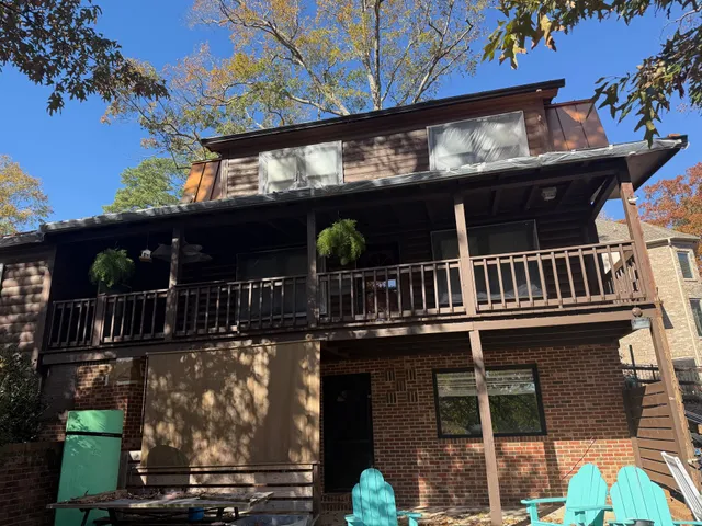 Two-story cabin with brown wood and brick exterior, balconies, and hanging plants.