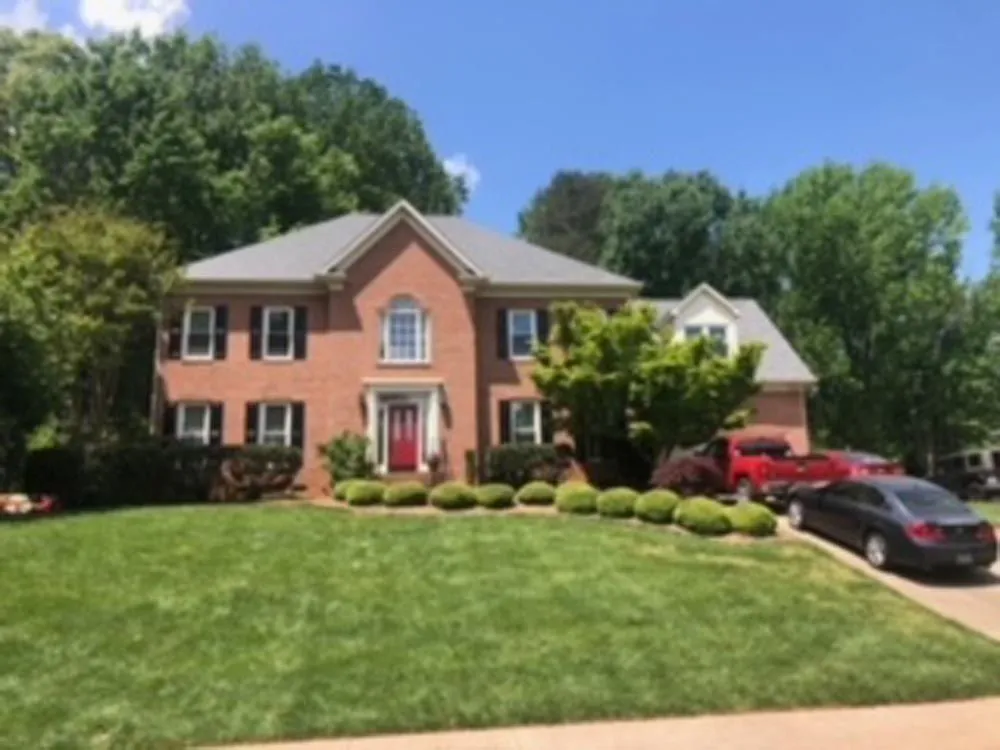 Two-story brick house with a red front door, black shutters, and well-manicured lawn on a sunny day.