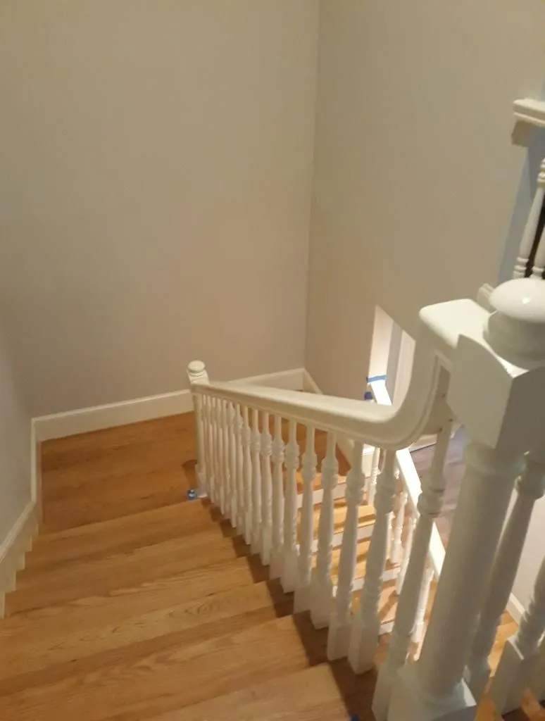 Wooden staircase with white banister, beige walls, and wood flooring.