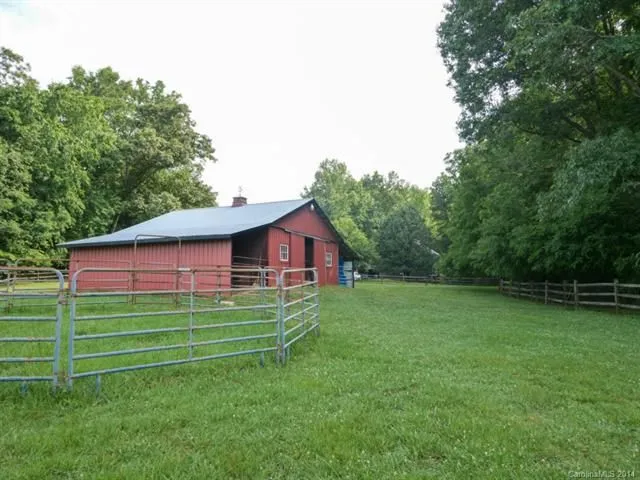 Red barn with green field, fence, and trees. Blue door.