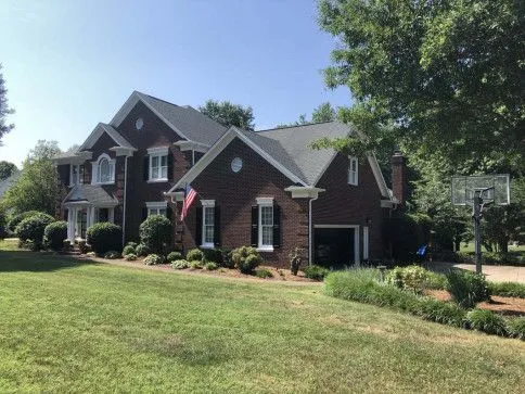 Brick house with black roof, white trim, and American flag on the front. Garage and basketball hoop visible.