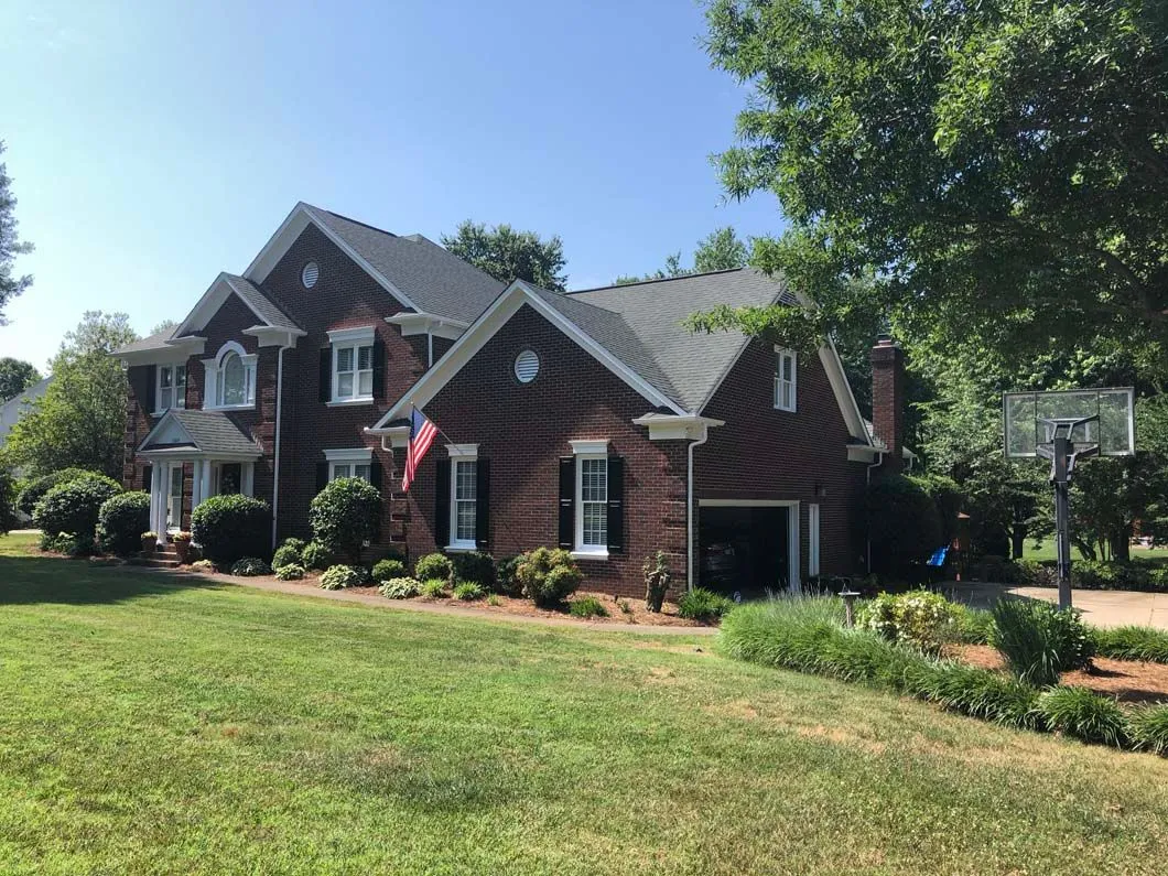 Two-story brick house with a green lawn, windows, and an American flag.