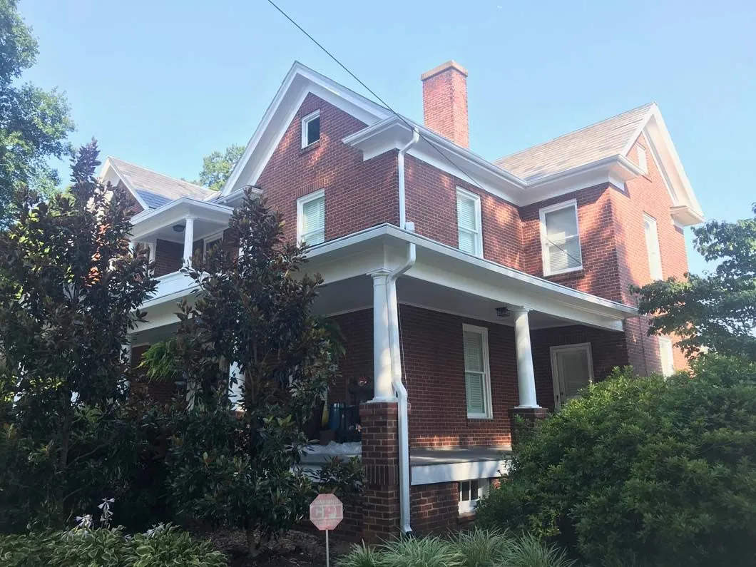 Red brick two-story house with white trim, porch, and a chimney against a blue sky.