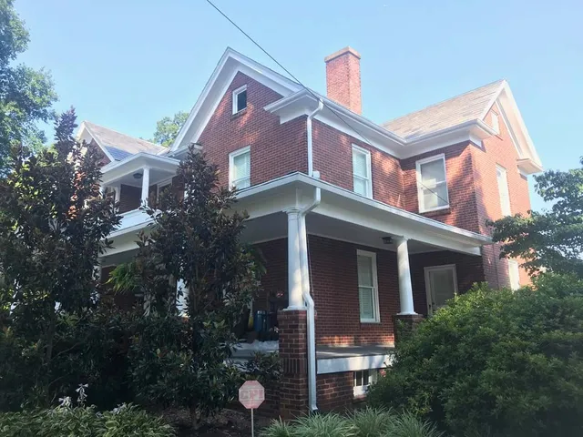 Red brick two-story house with white trim, porch, and a chimney against a blue sky.