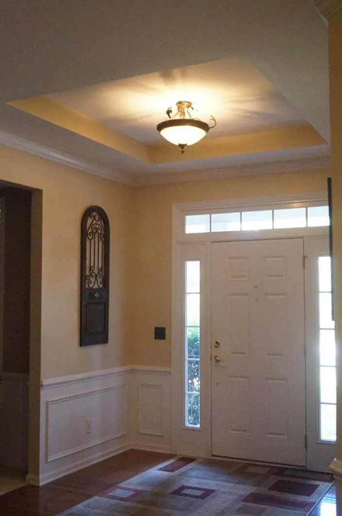 Entryway with white door, light fixture, beige walls, and wood floor.