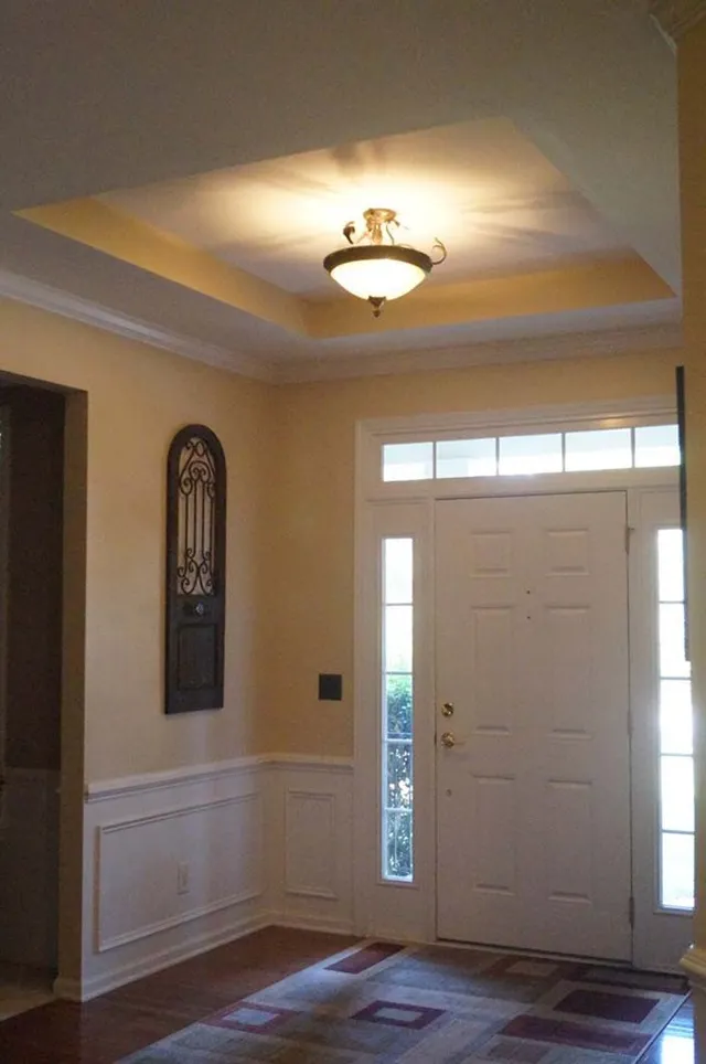 Entryway with white door, light fixture, beige walls, and wood floor.