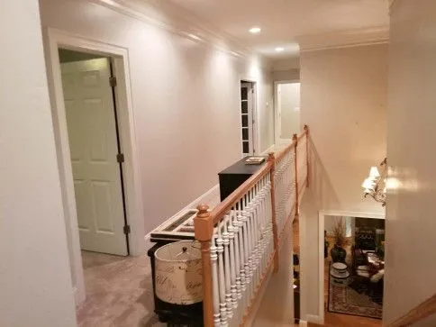 Hallway with stairs and multiple doorways, lit with overhead lights. Cream-colored walls, white trim.