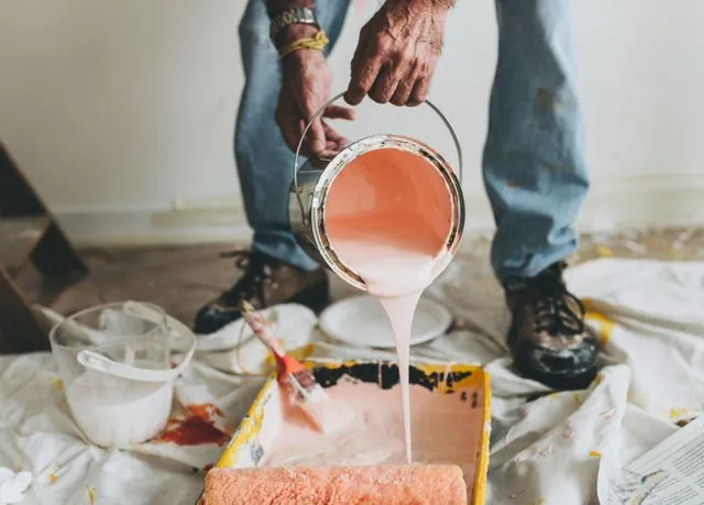 Person pouring pink paint into a paint tray. Interior setting.