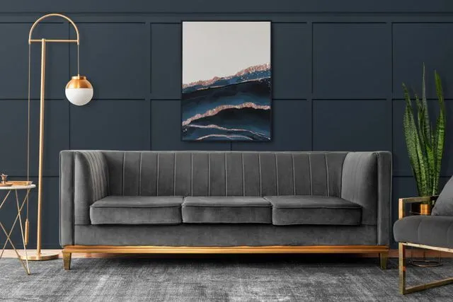 Gray velvet sofa in a room with navy walls, gold accents, and artwork.