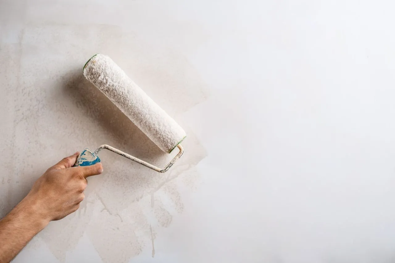 Hand holding a paint roller applying white paint to a wall.