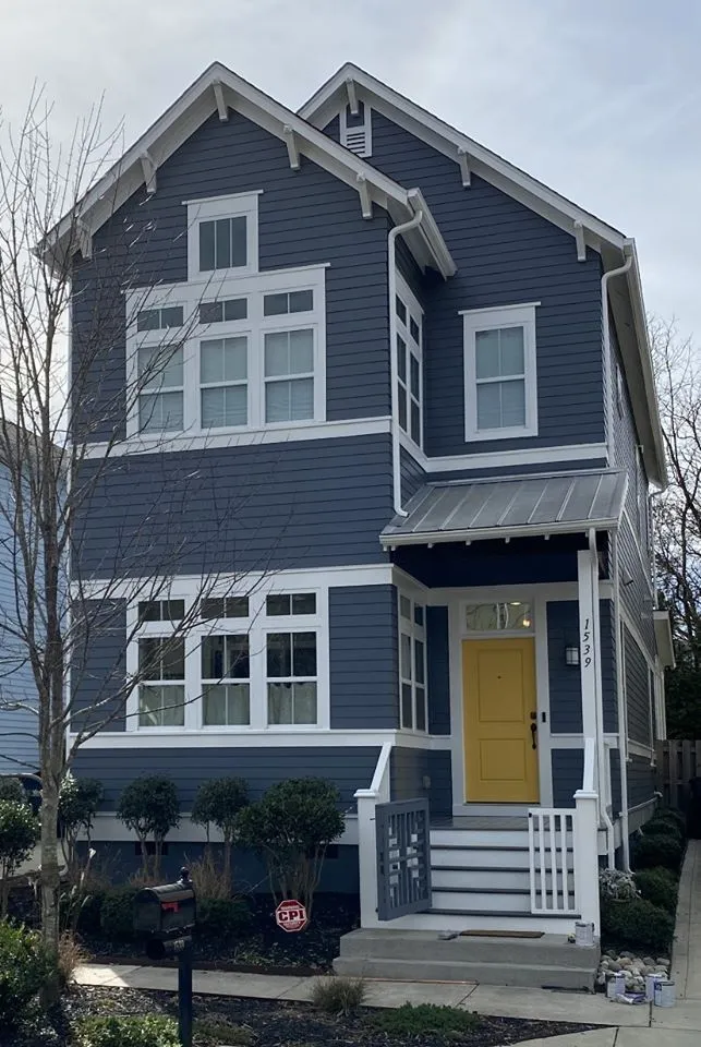 Two-story blue house with white trim and a yellow front door. Porch with metal roof.