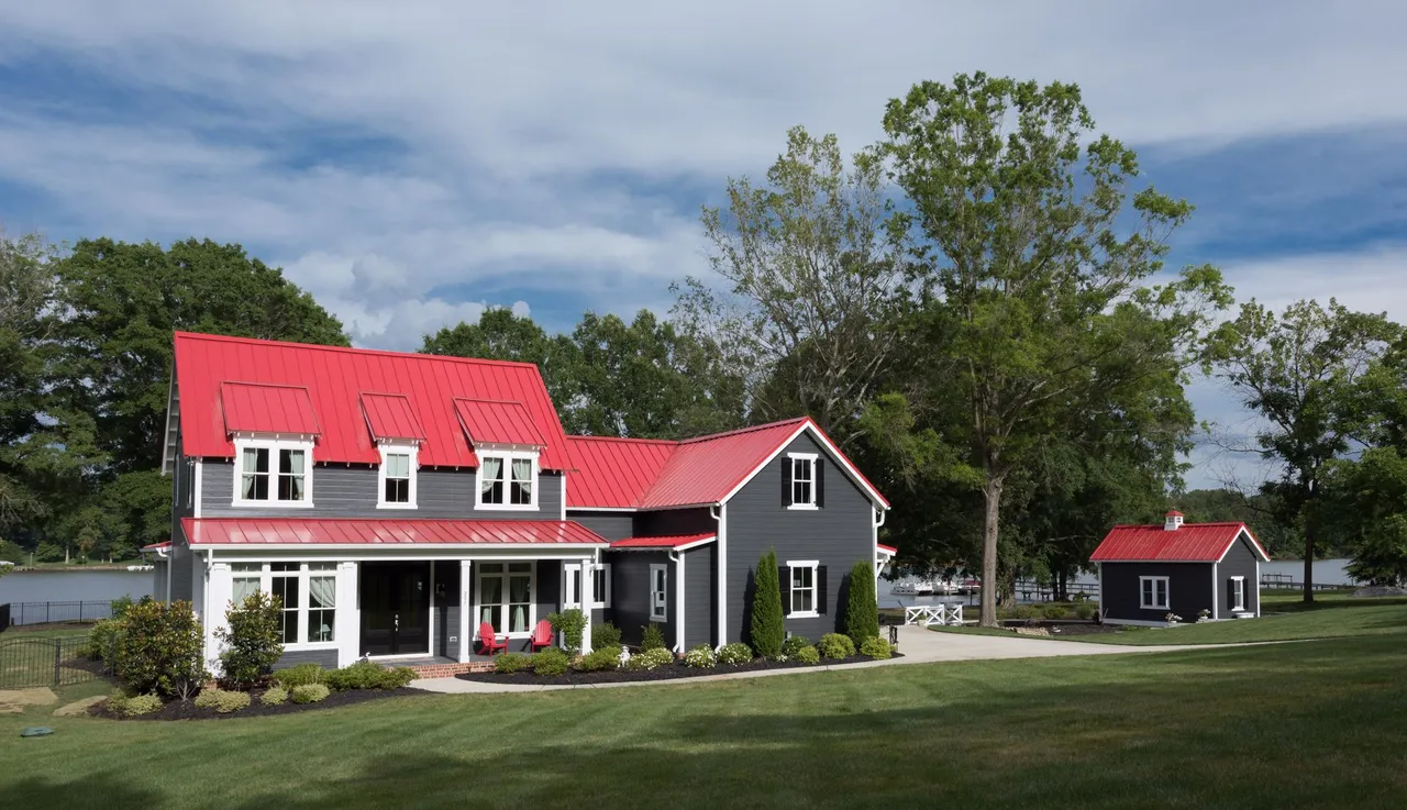 Gray house with red roof, small outbuilding, and green lawn under a blue sky.