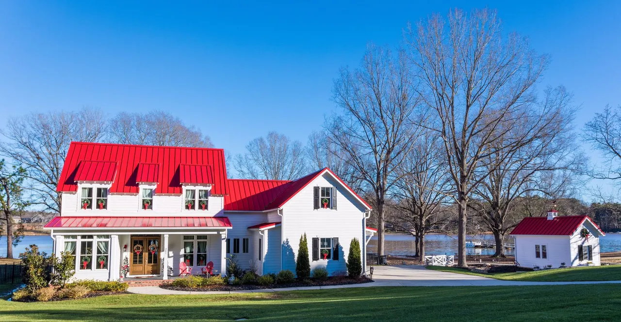 White farmhouse with bright red roof; sunny day by water.