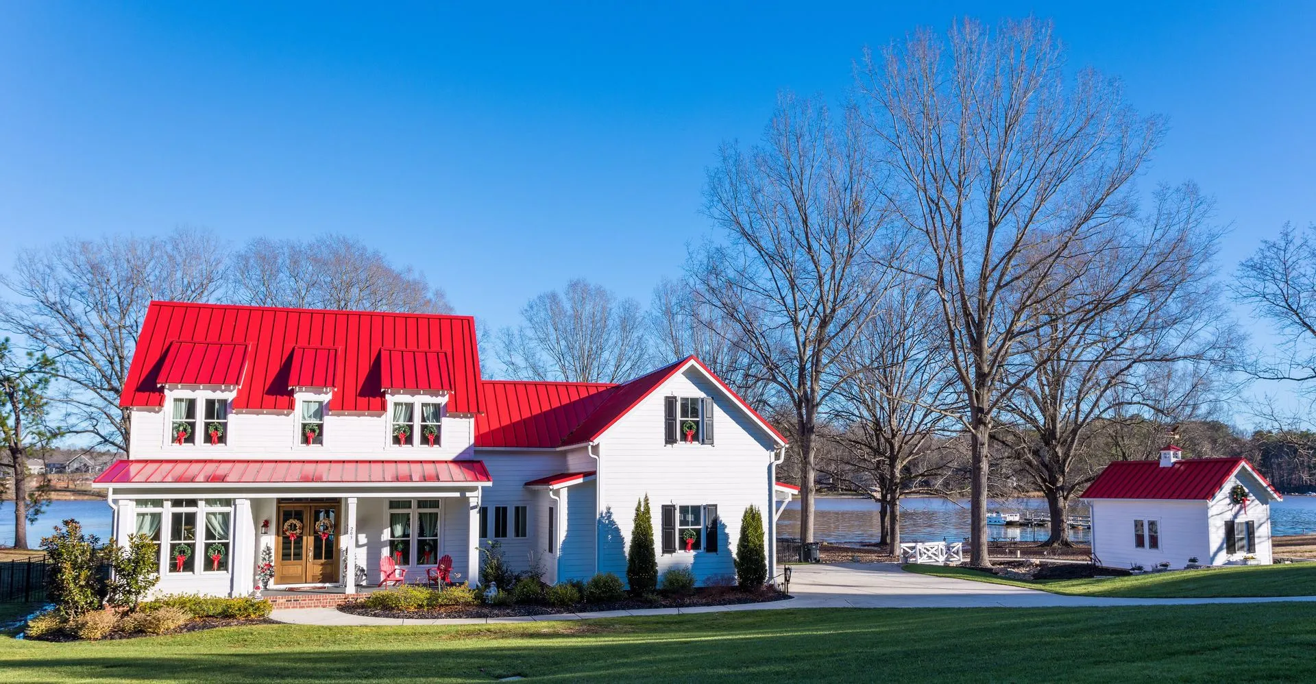White farmhouse with bright red roof; sunny day by water.